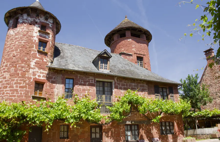 A majestic red sandstone manor with two towers and green vines in Collonges-la-Rouge, France.
