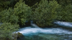 Long exposure fine art photography of the Sorgue river in Fontaine-de-Vaucluse, France, featuring emerald green water and silky white stream motion surrounded by wild trees and forest foliage.