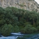 Long exposure landscape photography of the massive limestone cliffs and dense woodland canyon overlooking the emerald waters of the Sorgue river in Fontaine-de-Vaucluse, France.