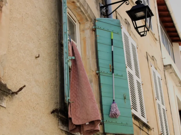 A rustic turquoise wooden shutter with a classic black iron lantern on a warm stucco facade in Tarascon, Provence.