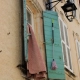 A rustic turquoise wooden shutter with a classic black iron lantern on a warm stucco facade in Tarascon, Provence.