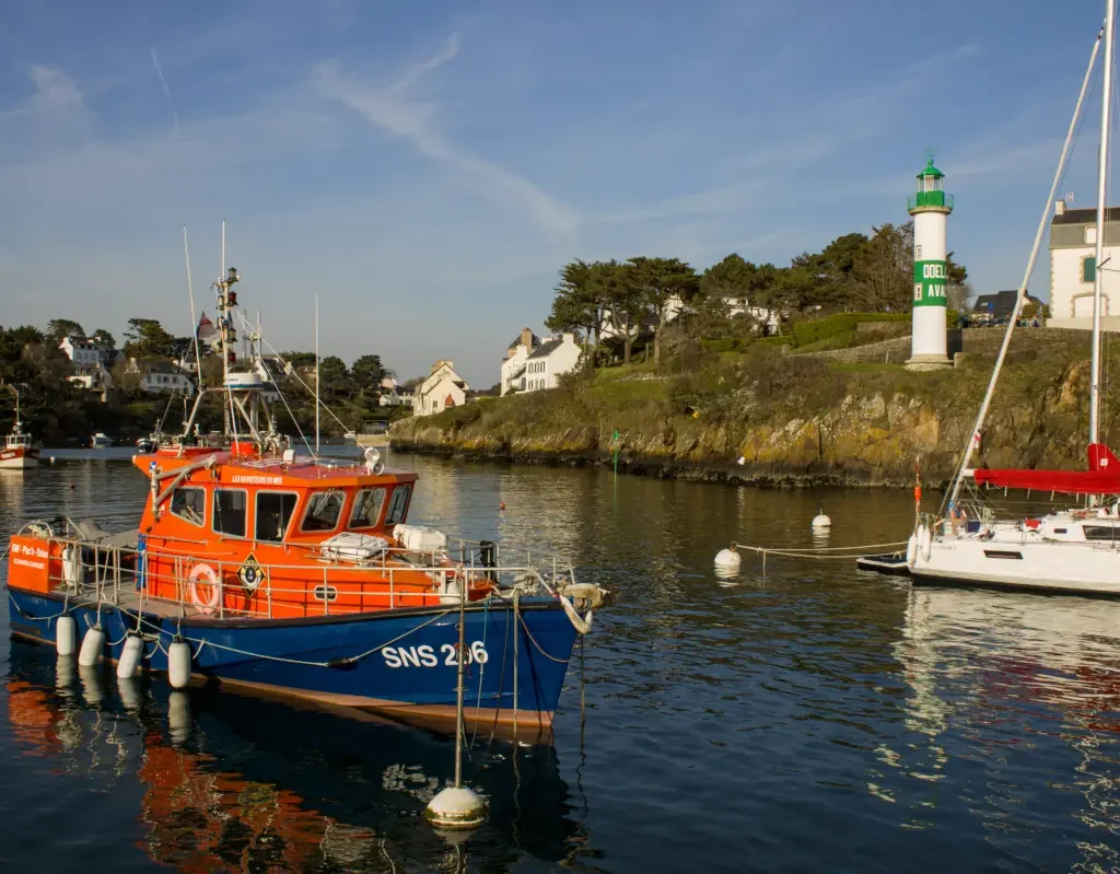 Rescue boat SNS 206 moored in a scenic harbor with a lighthouse and coastal houses in the background