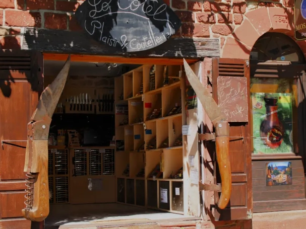 Giant wooden pocket knives used as window shutters on a traditional red sandstone knife shop in Collonges-la-Rouge, France.