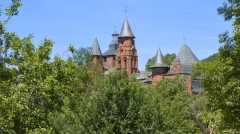 Red stone towers of Collonges-la-Rouge emerging from green trees under a blue sky.