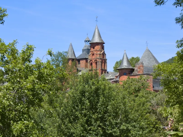 Red stone towers of Collonges-la-Rouge emerging from green trees under a blue sky.