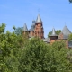 Red stone towers of Collonges-la-Rouge emerging from green trees under a blue sky.