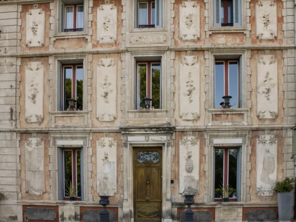 Historic ochre facade with floral frescoes and a carved wooden door in Fontaine-de-Vaucluse.