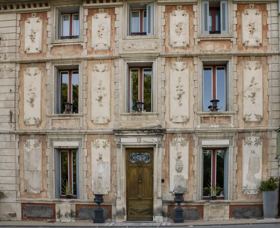 Historic ochre facade with floral frescoes and a carved wooden door in Fontaine-de-Vaucluse.