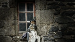 Witch doll sitting on a rustic stone window sill in the medieval village of Salers, France.